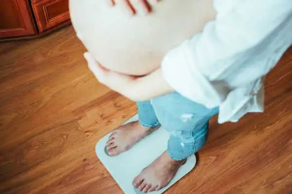 Image of woman weighing herself and experiencing weight gain through pregnancy Shepperton Green